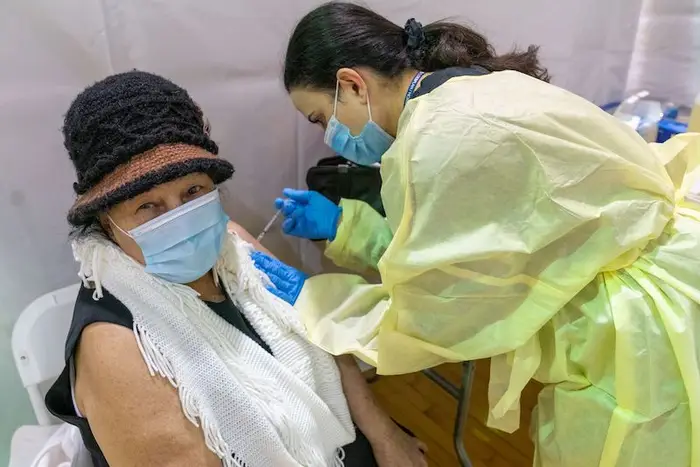 Registered Nurse Rita Alba wearing a mask and yellow gown gives a masked senior citizen the first dose of the coronavirus vaccine at a pop-up COVID-19 vaccination site at the Bronx River Community Center.